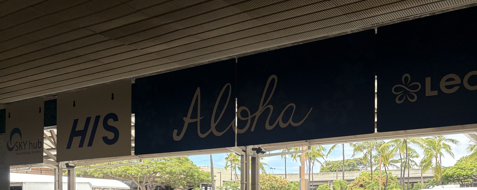 ダニエル・K・イノウエ国際空港のLeaLeaシャトル乗り場。HISとLeaLeaの看板、Alohaのサイン、奥にヤシの木